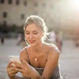 Donna sorride guardando il suo smartphone, forse prenotando un b&b per le vacanze. Luce dorata del tramonto.