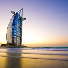 Iconico 7 sterne hotel Dubai, il Burj Al Arab, si staglia sulla spiaggia al tramonto, con onde che lambiscono la riva.