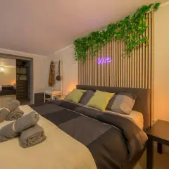 Camera da letto moderna con piante rampicanti, neon "love" e asciugamani arrotolati, perfetta per un booking fotografico.
