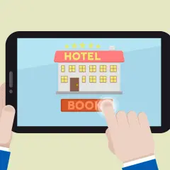 Un dito tocca il pulsante "BOOK" su un tablet che mostra un hotel stilizzato, simbolo dei siti internet hotel per prenotazioni facili.