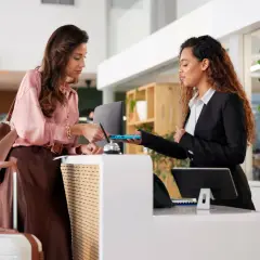 Donna effettua il check-in in hotel, mostrando il suo documento alla receptionist. L'orario del check-in è rispettato.