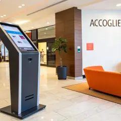 Chiosco per check in automatico b&b. Accoglienza smart con divani arancioni e piante.