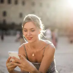 Donna sorride guardando il suo smartphone, forse prenotando un b&b per le vacanze. Luce dorata del tramonto.