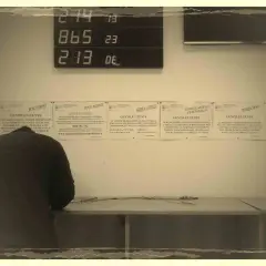 Un uomo si china su un tavolo, mentre sullo sfondo un display digitale mostra numeri. Informazioni su "codice univoco cos'è" e altri servizi sono affisse ai muri.