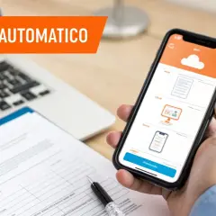 Mano che tiene uno smartphone con app per invio automatico, accanto a un laptop e documenti.