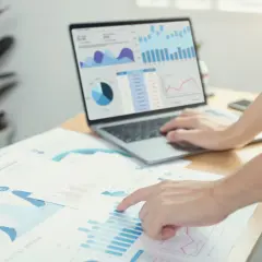 Analisi di grafici e dati di prima parte su un laptop e fogli di carta, con mani che interagiscono con i report.