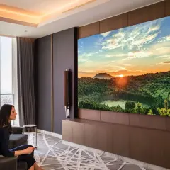 Donna guarda un tramonto mozzafiato su un'enorme hospitality tv, godendosi il comfort del suo soggiorno.