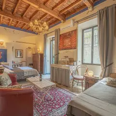 Camera accogliente in un hotel o b&b con soffitto in legno, divano rosso, due letti e un lavabo decorato.