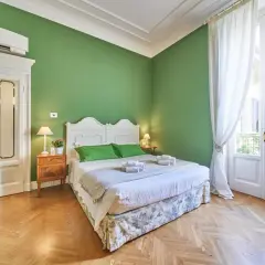 Camera da letto accogliente con pareti verdi, letto bianco, tende bianche e parquet. Ideale per capire la differenza tra foresteria e B&B.