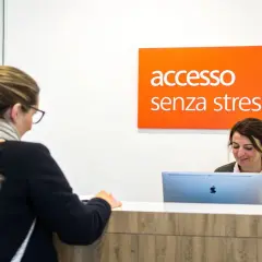 Una donna alla reception, con un cartello "accesso senza stress" sopra, sembra avere problemi con il suo computer.