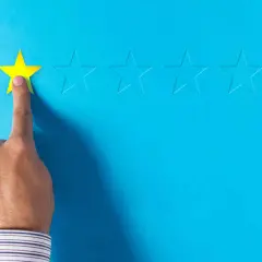 Dito, una mano seleziona una stella gialla, lasciando le altre vuote. Un'immagine che evoca le recensioni negative sui booking.