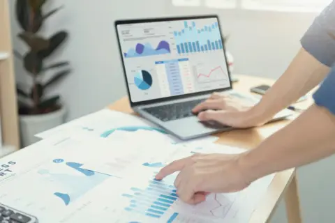 Analisi di grafici e dati di prima parte su un laptop e fogli di carta, con mani che interagiscono con i report.
