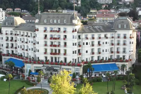 Hotel Regina Palace, un'elegante struttura con balconi fioriti. Forse stanno facendo un **ab testing** per vedere quale colore di tende blu attira più clienti.
