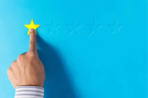 Dito, una mano seleziona una stella gialla, lasciando le altre vuote. Un'immagine che evoca le recensioni negative sui booking.