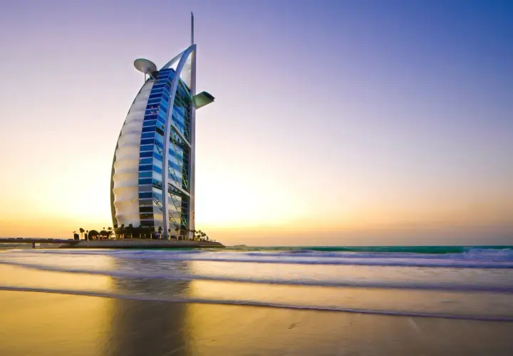 Iconico 7 sterne hotel Dubai, il Burj Al Arab, si staglia sulla spiaggia al tramonto, con onde che lambiscono la riva.
