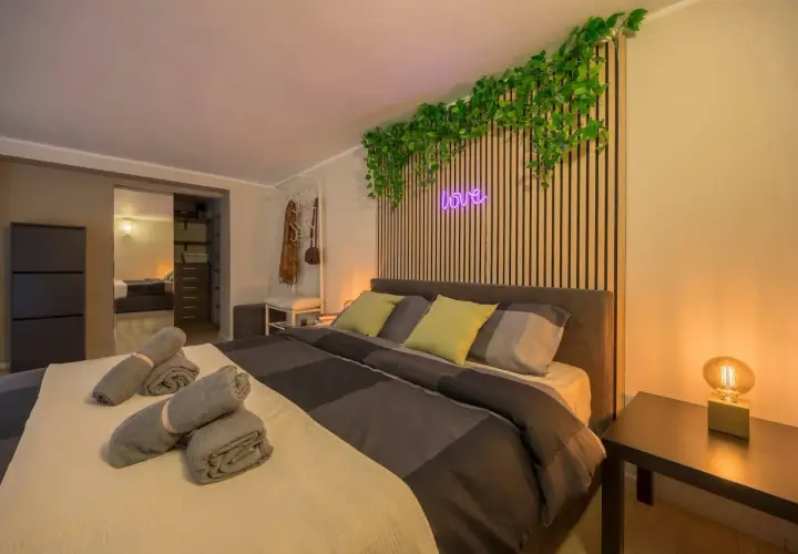 Camera da letto moderna con piante rampicanti, neon "love" e asciugamani arrotolati, perfetta per un booking fotografico.