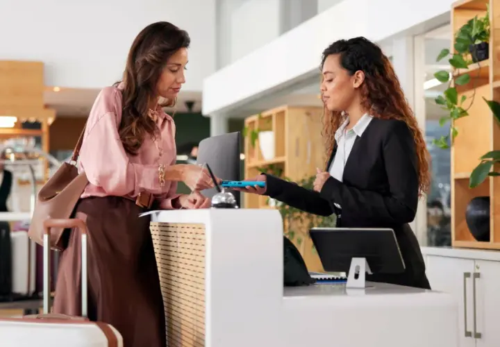Donna effettua il check-in in hotel, mostrando il suo documento alla receptionist. L'orario del check-in è rispettato.