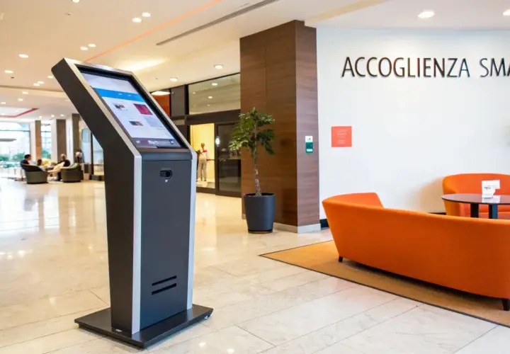 Chiosco per check in automatico b&b. Accoglienza smart con divani arancioni e piante.