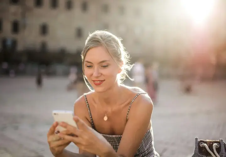 Donna sorride guardando il suo smartphone, forse prenotando un b&b per le vacanze. Luce dorata del tramonto.