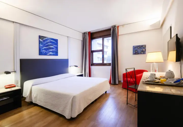 Camera accogliente con letto, poltrona rossa e vassoio colazione, perfetta per un day use rilassante.
