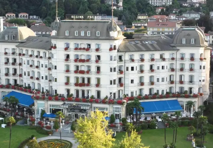 Hotel Regina Palace, un'elegante struttura con balconi fioriti. Forse stanno facendo un **ab testing** per vedere quale colore di tende blu attira più clienti.