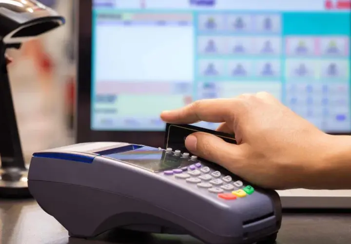 Pagamento con carta su POS, con registratore di cassa sullo sfondo.