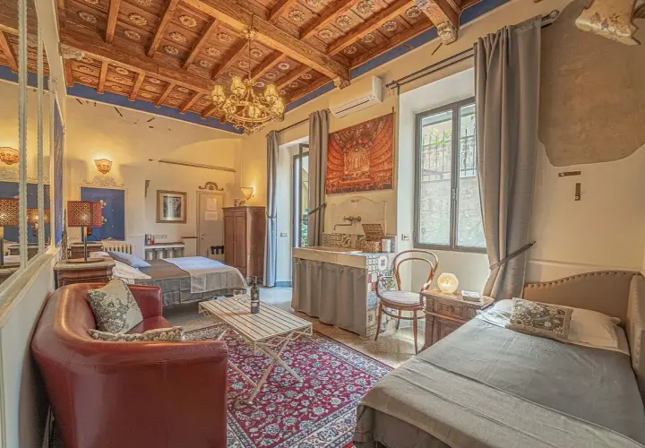Camera accogliente in un hotel o b&b con soffitto in legno, divano rosso, due letti e un lavabo decorato.