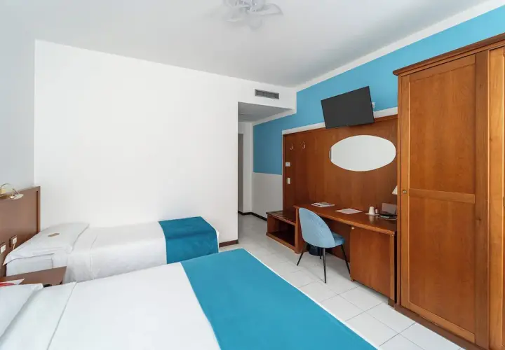 Camera d'albergo con due letti singoli, scrivania e armadio. Ottima per la valutazione hotel.