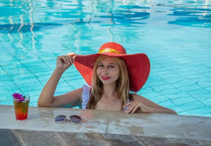 Donna con cappello rosso in piscina, sorseggia un cocktail. Cosa significa guest? Essere coccolati e rilassati, proprio come lei.