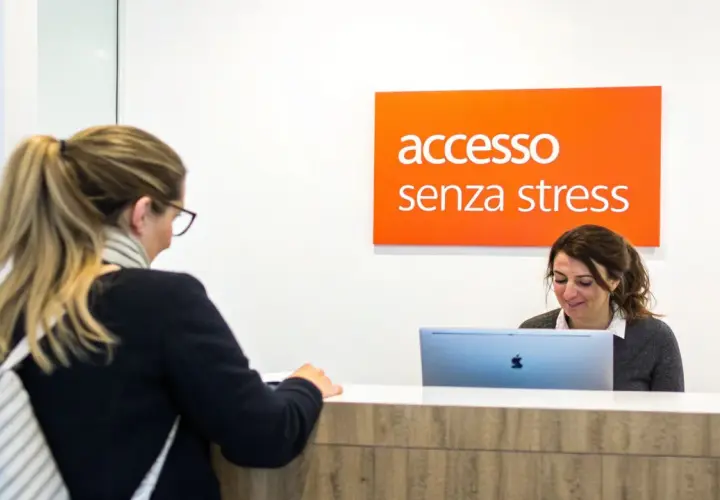 Una donna alla reception, con un cartello "accesso senza stress" sopra, sembra avere problemi con il suo computer.
