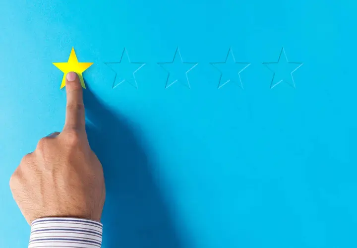 Dito, una mano seleziona una stella gialla, lasciando le altre vuote. Un'immagine che evoca le recensioni negative sui booking.