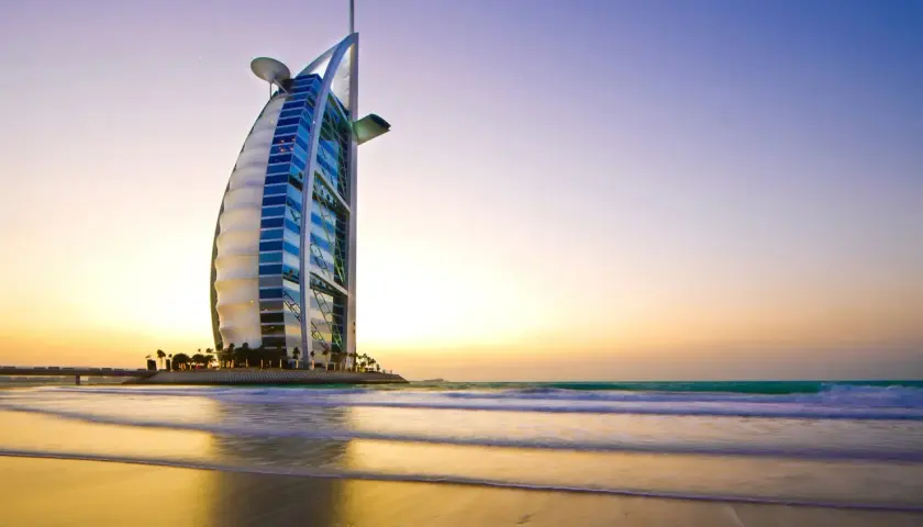 Iconico 7 sterne hotel Dubai, il Burj Al Arab, si staglia sulla spiaggia al tramonto, con onde che lambiscono la riva.