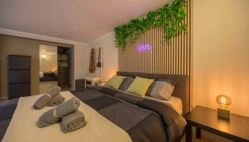 Camera da letto moderna con piante rampicanti, neon "love" e asciugamani arrotolati, perfetta per un booking fotografico.