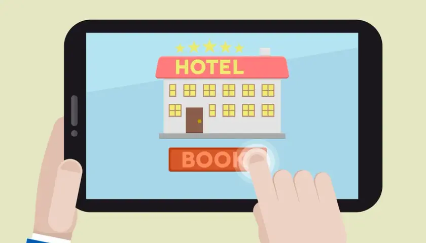 Un dito tocca il pulsante "BOOK" su un tablet che mostra un hotel stilizzato, simbolo dei siti internet hotel per prenotazioni facili.