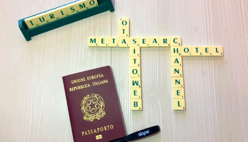 Un passaporto italiano, tessere di parole che formano "METASEARCH", "TURISMO", "HOTEL" e "CHANNEL". Strumenti per pianificare viaggi tramite metamotori di ricerca.