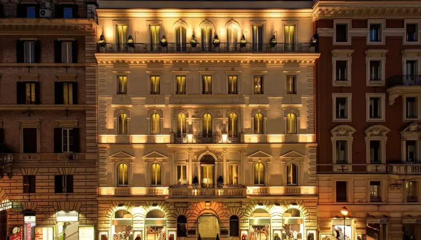 Edificio illuminato di notte, con negozi al piano terra. Si percepisce la differenza tra hotel 3 stelle e 4 stelle dall'eleganza.