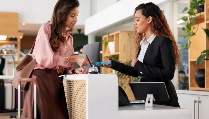 Donna effettua il check-in in hotel, mostrando il suo documento alla receptionist. L'orario del check-in è rispettato.