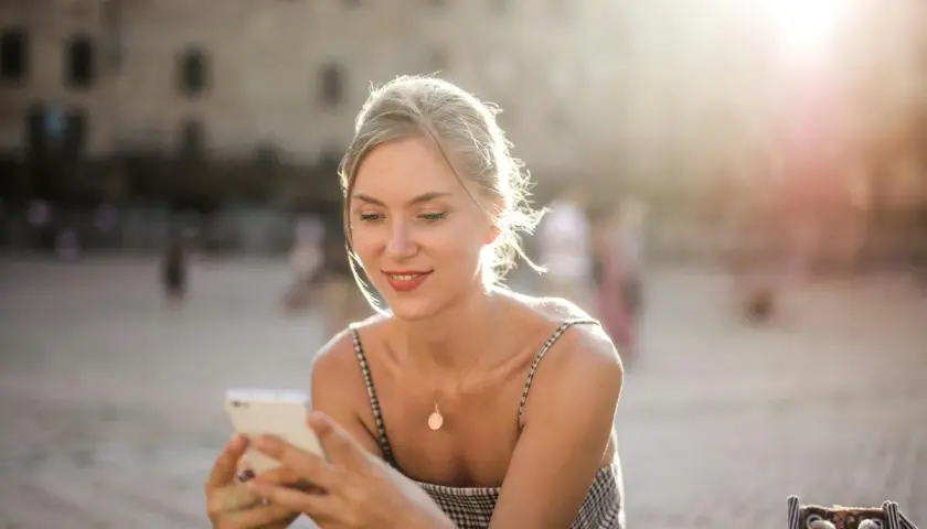 Donna sorride guardando il suo smartphone, forse prenotando un b&b per le vacanze. Luce dorata del tramonto.