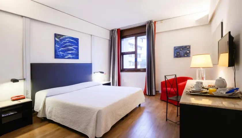Camera accogliente con letto, poltrona rossa e vassoio colazione, perfetta per un day use rilassante.