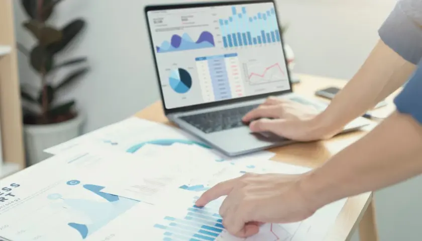 Analisi di grafici e dati di prima parte su un laptop e fogli di carta, con mani che interagiscono con i report.