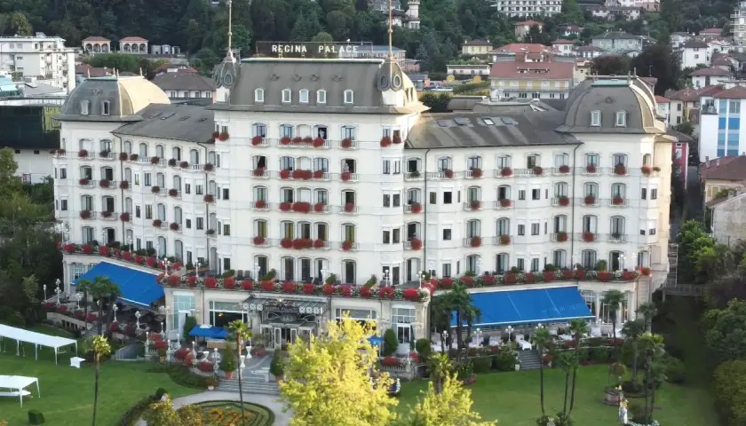 Hotel Regina Palace, un'elegante struttura con balconi fioriti. Forse stanno facendo un **ab testing** per vedere quale colore di tende blu attira più clienti.