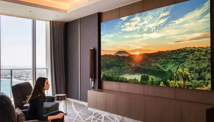Donna guarda un tramonto mozzafiato su un'enorme hospitality tv, godendosi il comfort del suo soggiorno.