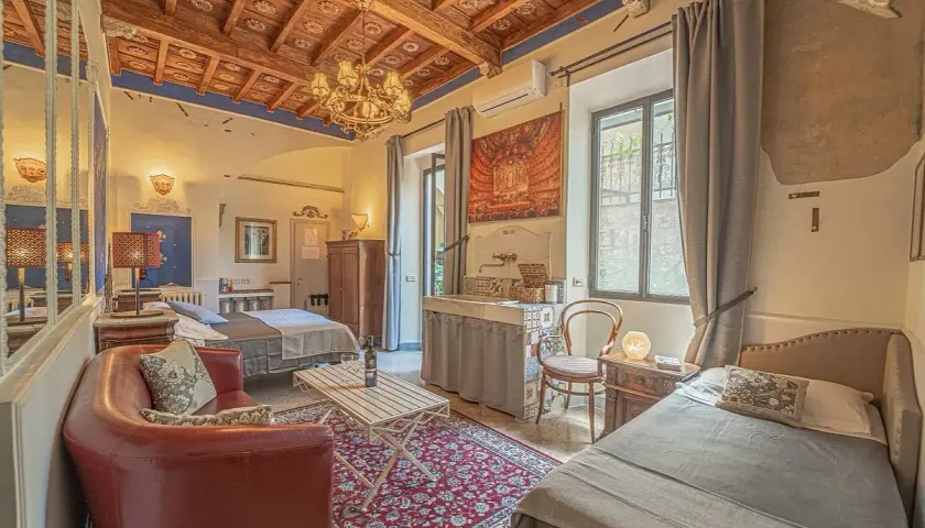 Camera accogliente in un hotel o b&b con soffitto in legno, divano rosso, due letti e un lavabo decorato.