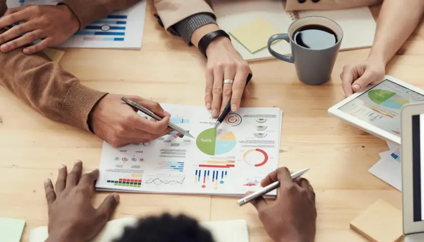 Persone analizzano grafici e dati su un tavolo, discutendo le impostazioni OTA (Over-The-Air) per aggiornamenti software.
