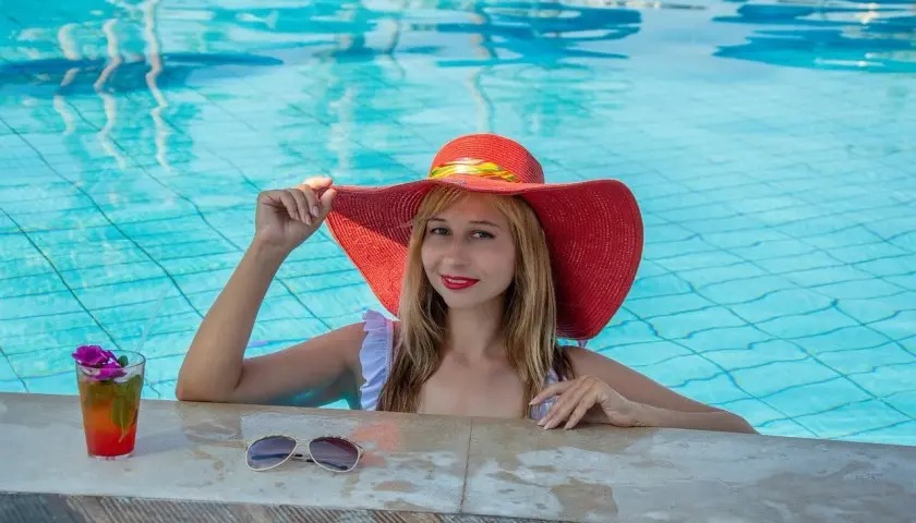 Donna con cappello rosso in piscina, sorseggia un cocktail. Cosa significa guest? Essere coccolati e rilassati, proprio come lei.