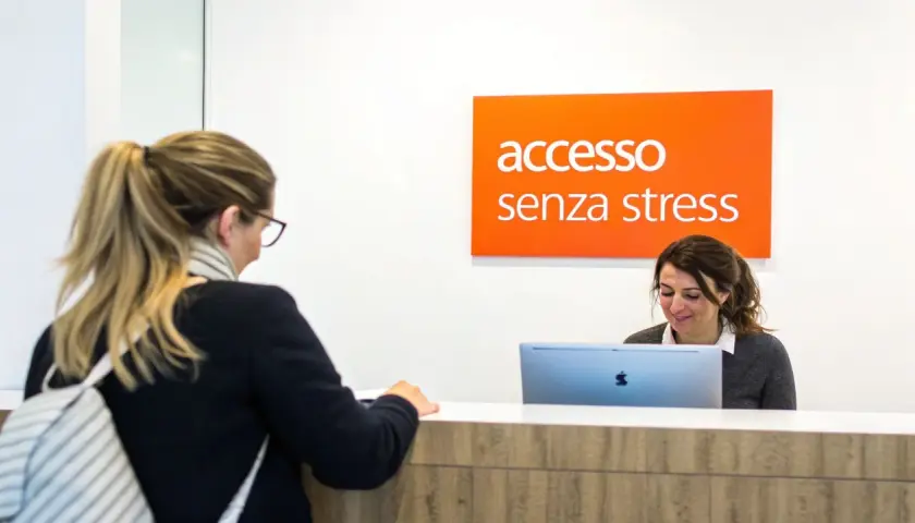 Una donna alla reception, con un cartello "accesso senza stress" sopra, sembra avere problemi con il suo computer.