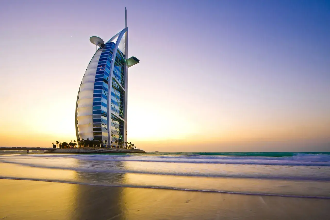 Iconico 7 sterne hotel Dubai, il Burj Al Arab, si staglia sulla spiaggia al tramonto, con onde che lambiscono la riva.