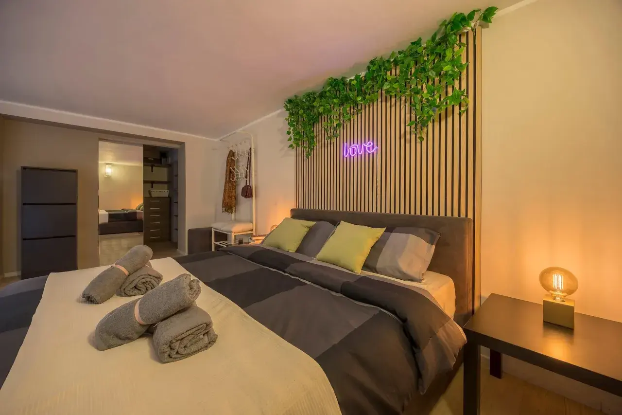 Camera da letto moderna con piante rampicanti, neon "love" e asciugamani arrotolati, perfetta per un booking fotografico.