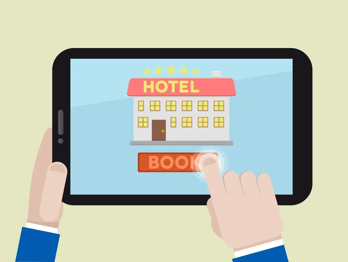 Un dito tocca il pulsante "BOOK" su un tablet che mostra un hotel stilizzato, simbolo dei siti internet hotel per prenotazioni facili.