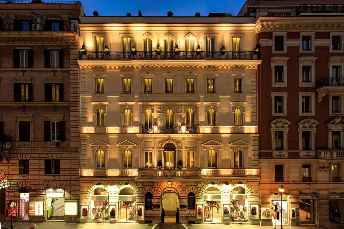 Edificio illuminato di notte, con negozi al piano terra. Si percepisce la differenza tra hotel 3 stelle e 4 stelle dall'eleganza.